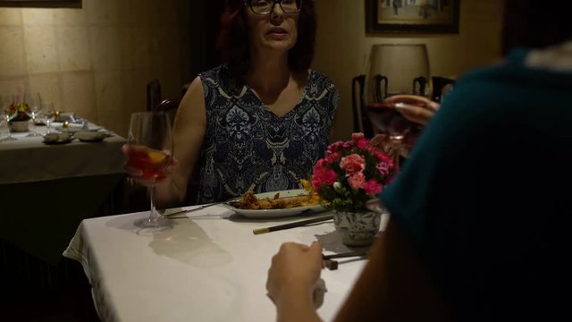 In the restaurant, a woman sitting at a table, eating, talking, clink glasses and drink red wine