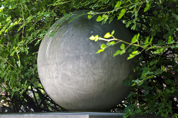 A rounds stone globe in the bushes of the forest woodland area in the summer heat.