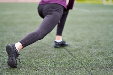 Fototapeta premium Woman stretching. Young female workout before fitness training session on a football field. Healthy young woman warming up outdoors.