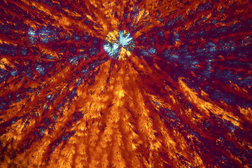 Abstract micrograph of orange and blue lysine crystals.