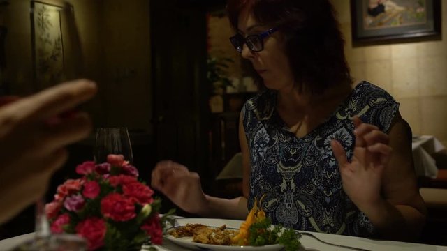 Women sitting at a table in a restaurant, eating, talking, clink glasses and drink red wine