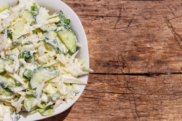 Spring salad with cabbage, cucumber, green onion, parsley and mayonnaise on wooden table