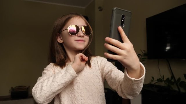 Funny cute kid girl portrait at home takes mobile phone selfie picture opening her face from hairs