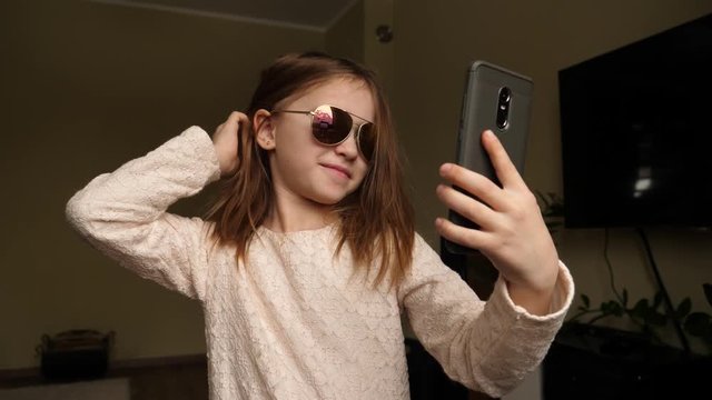 Funny cute kid girl portrait at home takes mobile phone selfie picture opening her face from hairs