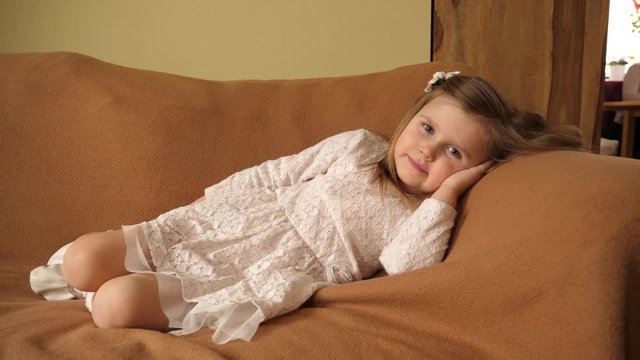 Little cute girl child in white dress at home rest lie on a couch rug