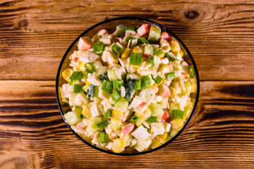 Glass bowl with salad from crab sticks on wooden table. Top view