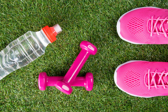 pink sneakers, dumbbells for fitness and a bottle of water, against the background of grass