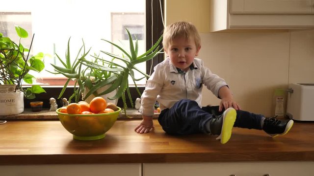 Little boy child at home crawling playing on kitchen countertop with fruits in bowl