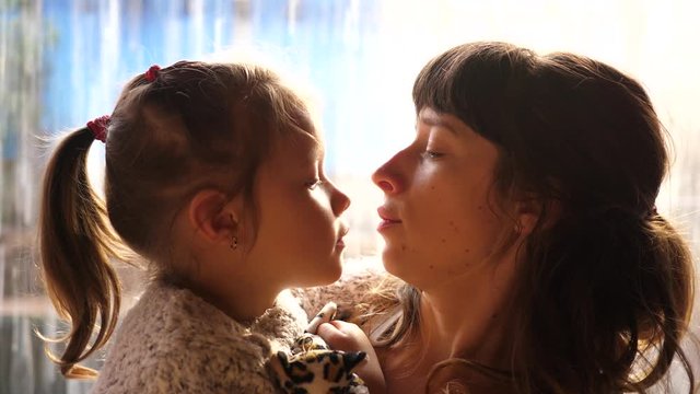 Young mother holds hug and kiss her little kid daughter on hands - tender family portrait