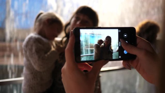 Take mobile phone pictures of young mother holds hug and kiss her little kid daughter on hands