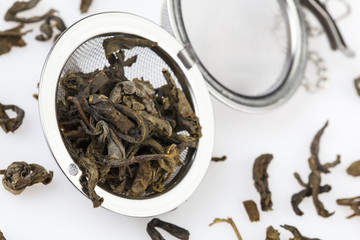 Tea strainer on a chain, with green tea, isolated on a white background.