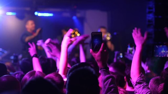 Smart phones in hands spectators crowd dance jump and shoot video of concert performance