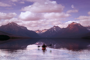 Adventurer paddling on mountain lake during morning sunrise, with beautiful scenic reflection of...