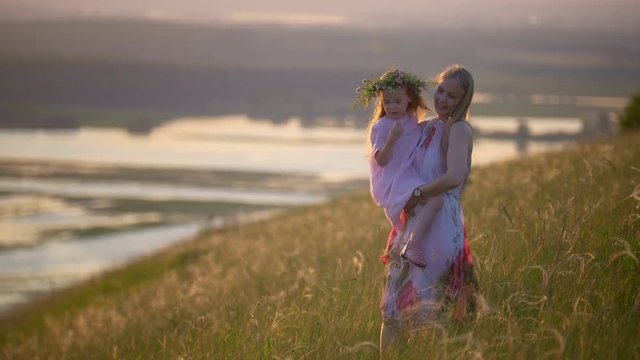 Young mother holding daughter in arms walks down the hill at summer sunset
