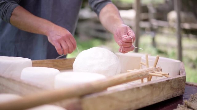 The process of making cheese. The homemade cheese producer in the Alps Mountains combines milk, forms and cuts cheese into two parts to put them in wooden forms