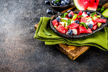 Summer food concept, fresh cold watermelon salad with feta cheese, blueberry, avocado and mint, dark rusty background copy space