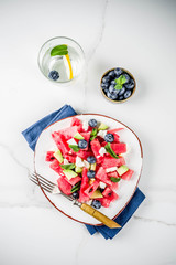 Obraz na płótnie Canvas Summer food concept, fresh cold watermelon salad with feta cheese, blueberry, avocado and mint, white marble background copy space