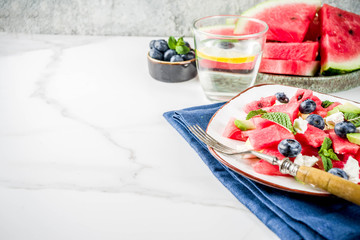 Summer food concept, fresh cold watermelon salad with feta cheese, blueberry, avocado and mint, white marble background copy space
