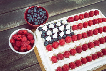 Patriotic, red white and blue, American flag cake with fresh raspberries and blueberries on rustic wooden table. 