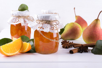 Pear and orange jam in  glass jars with ripe pears, cinnamon sticks, anise stars and green  leaves on the table.