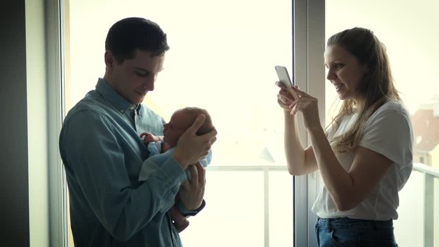 New parents hold newborn baby mother takes mobile phone pictures of father and son for social media