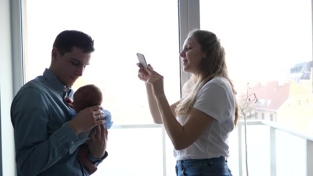New parents hold newborn baby mother takes mobile phone pictures of father and son for social media