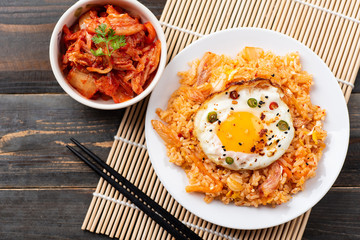 Kimchi fried rice with fried egg on top and fresh kimchi cabbage in a bowl, top view, Korean food