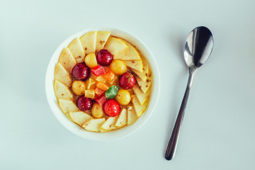 porridge with cherry, apple and candied fruits in white bowl on white background