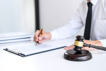 Businessman or lawyer working on a documents, judge gavel with Justice lawyers at law firm in background, Legal law, advice and justice concept
