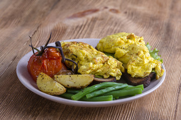 Egg omelette on a piece of black bread with red tomatoes, green beans and fried potato on a wooden table, close up. Breakfast concept