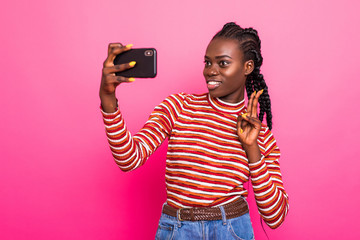 Beautiful woman making selfie on her cell phone with smile isolated over pink background