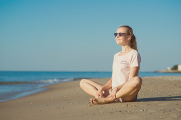 Young woman sitting on sand and doing yoga meditation on the beach