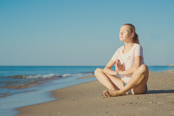 Fototapeta na wymiar Young woman sitting on sand and doing yoga meditation on the beach