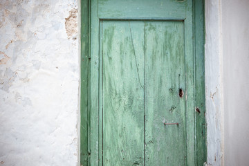 Old greenish blue wooden door and eroded white wall. Front door