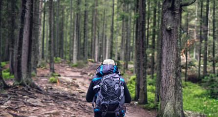 Young man with sports backpack travels in woods. Trek in the summer forest.