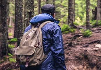 Young man with sports backpack travels in woods. Trek in the summer forest.