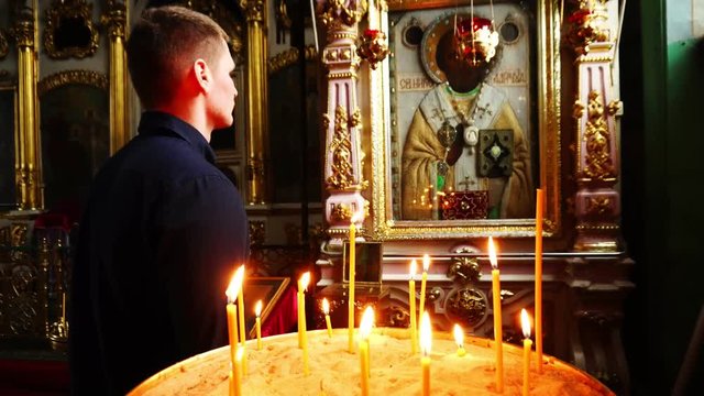 A man prays near the icon in the temple. In the foreground of the plan lit candles.