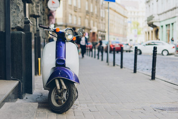 Obraz na płótnie Canvas Blue scooter on background of old city. Scooter parked on sidewalk of empty city street.