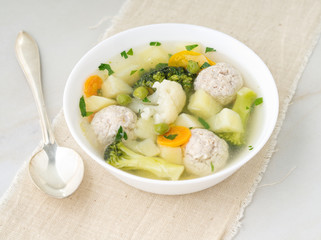 bowl of soup, a cup of broth and vegetables, meatballs made of turkey and chicken, side view