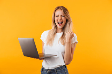 Portrait of an excited young blonde girl holding laptop - obrazy, fototapety, plakaty