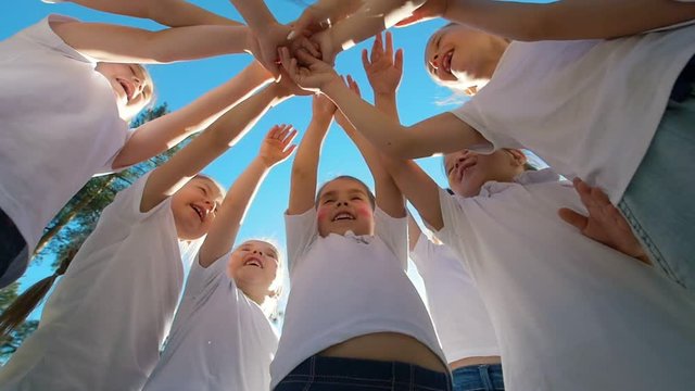Group of kids performs sports motivational greeting with hands on playground of yard football at sunny day