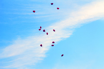 Red balls in the form of a heart fly into the blue sky.