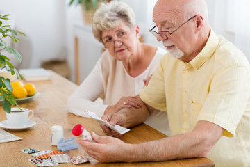 Elderly woman supporting sick senior man reading leaflet of drugs for hypertensive