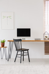 Simple interior of a home office with black chair standing at a wooden desk with an empty computer monitor. Real photo