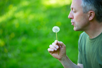 Man blowing dandelion over blured green grass, summer nature outdoor