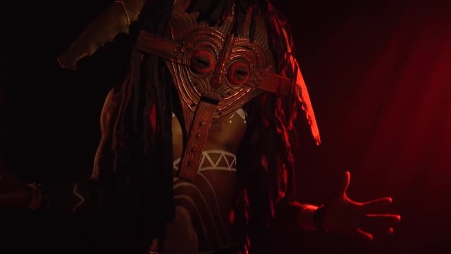 Black man in a wooden mask and white body art with ritual ornaments, conjures