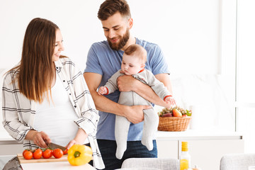 Happy parents with their baby son cooking in kitchen.