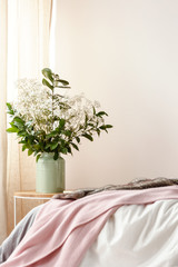 Photo with bed with pink blanket in blurred foreground and bedside table with flowers in green...