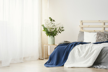 Navy blue blanket thrown on double bed with lights on bedhead standing in white bedroom interior...