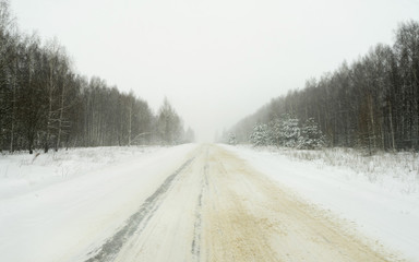 Vanishing snow-covered straight highway surrounded by winter forest recedes. Nizhegorodsky region, Russia.
